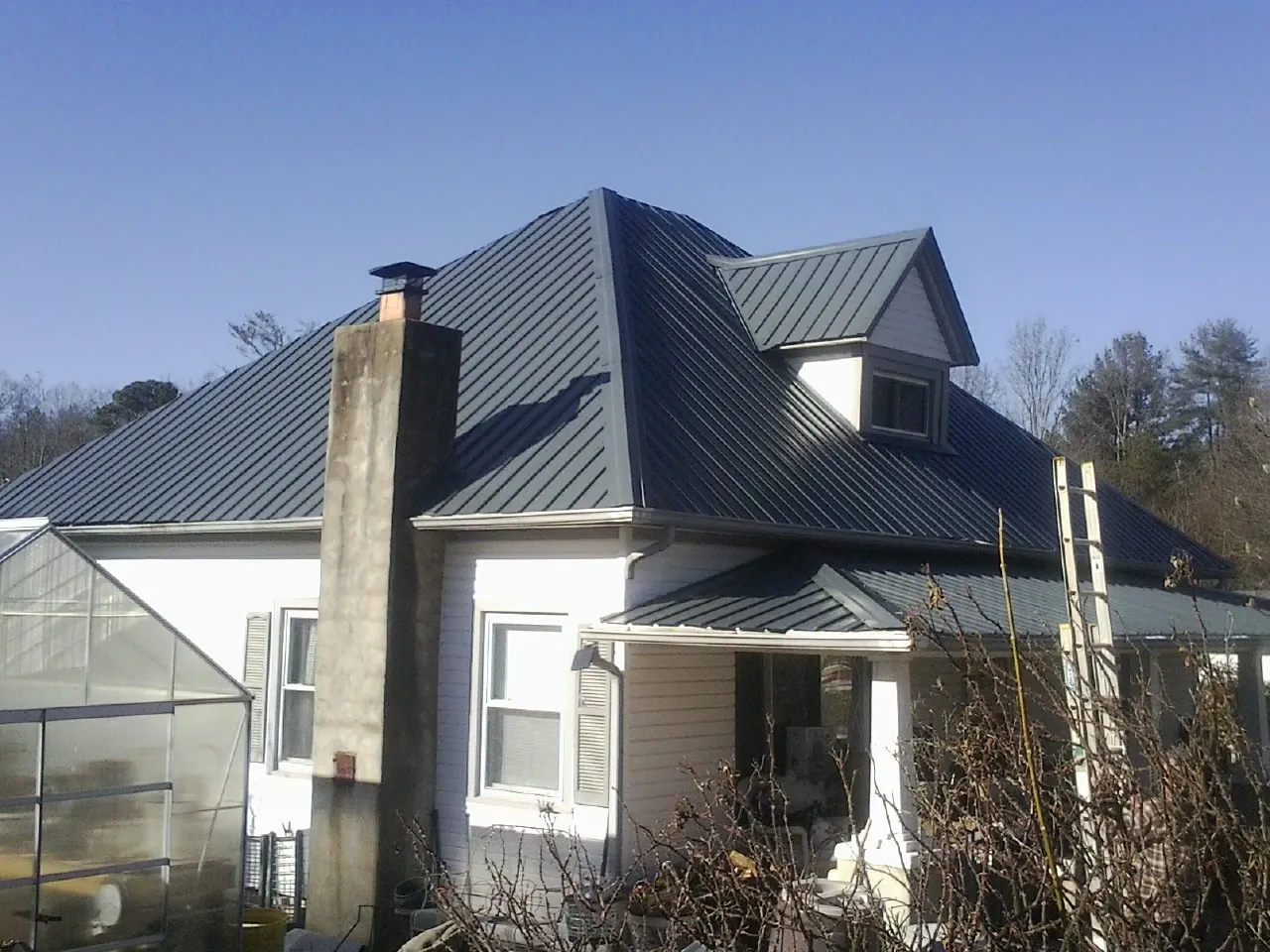 Dark blue standing seam metal roof on a white farmhouse with dormer — Slate & Tile Roof Repair by Roofing Brothers in Meridian