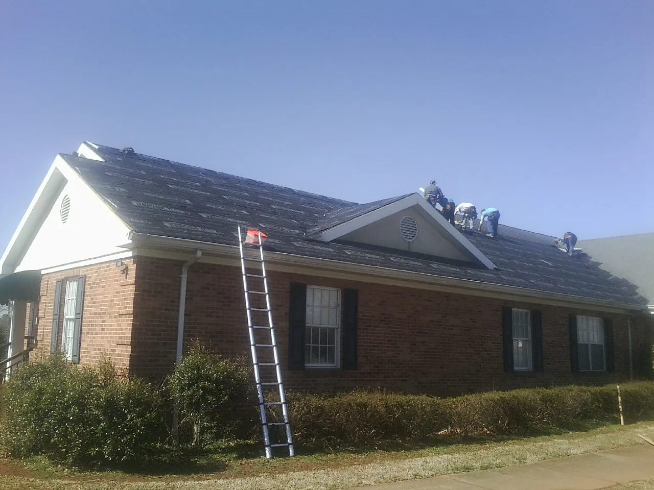 Crew tearing shingles off a brick ranch roof with a ladder set — Metal Roof Repair work by our crew in Meridian